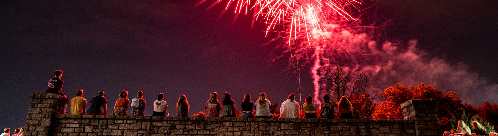 people sitting on a bridge watching fireworks