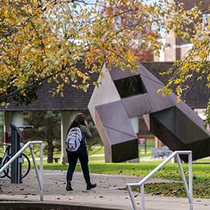 student walking on campus by the Cube sculpture in the fall
